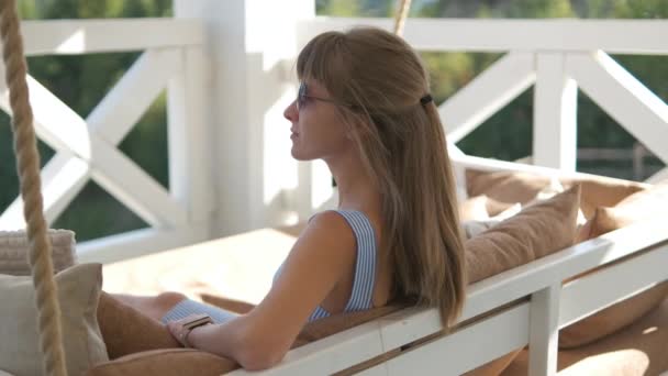 Giovane donna bruna felice sdraiata sul divano terrazza con morbidi cuscini godendo di una calda giornata estiva. Concetto di tempo libero all'aria aperta — Video Stock