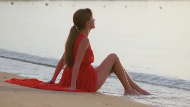 Young happy woman wearing red dress resting on sea beach enjoying warm summer morning — Stock Video