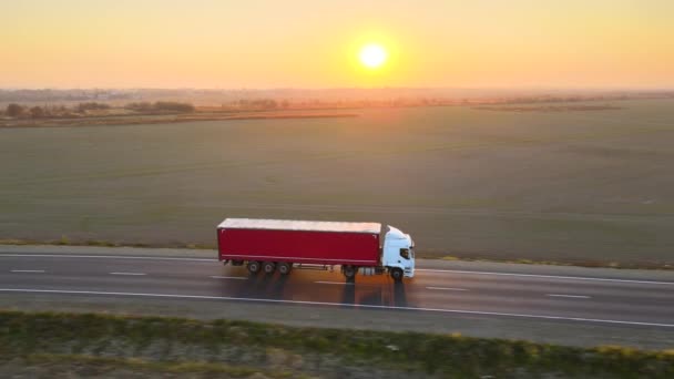 Flygfoto av semi-truck med last släpvagn kör på motorvägen transporterar varor på kvällen. Leveranstransport och logistikkoncept — Stockvideo
