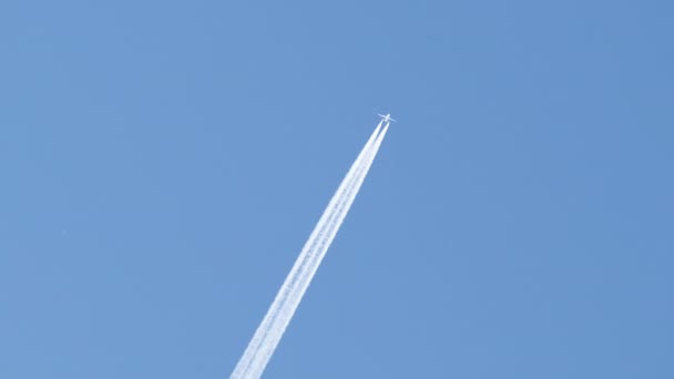 Oddalony odrzutowiec pasażerski lecący na dużej wysokości na bezchmurnym błękitnym niebie zostawiający za sobą biały ślad dymu. Koncepcja transportu lotniczego — Wideo stockowe