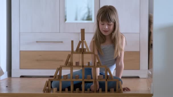 Ευτυχισμένο κορίτσι παιδί παίζει παιχνίδι Jenga στοίβαγμα ξύλινα μπλοκ παιχνιδιών σε υψηλή δομή σωρό. Χειροκίνητος έλεγχος κίνησης και δημιουργία υπολογιστικών δεξιοτήτων — Αρχείο Βίντεο
