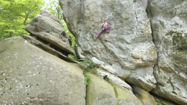 Mujer joven escalando empinada pared de montaña rocosa. Niña escaladora supera ruta desafiante. Participar en el concepto de deporte extremo — Vídeo de stock