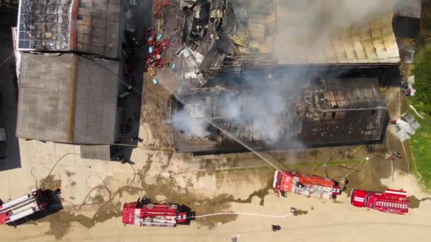 Повітряний вигляд пожежників, що гасять зруйновану будівлю під вогнем зруйнованого даху і піднімається темний дим — стокове відео