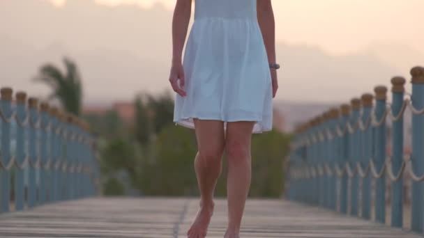 Close-up van jonge vrouw in witte jurk gaan voor een wandeling op lange pier aan zee in de avond. Vakantie en reizen concept — Stockvideo