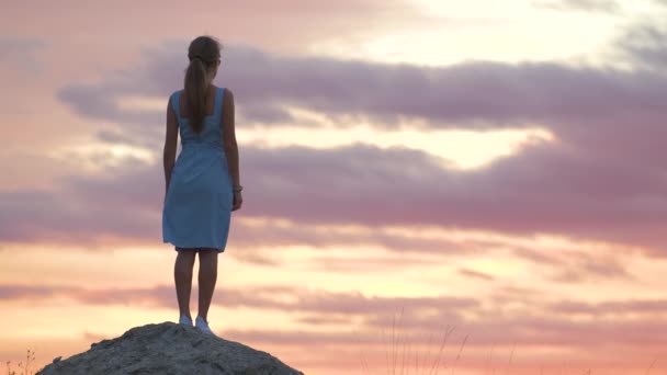 Donker silhouet van een jonge vrouw in zomerse jurk die buiten staat en geniet van het uitzicht op de natuur bij zonsondergang — Stockvideo