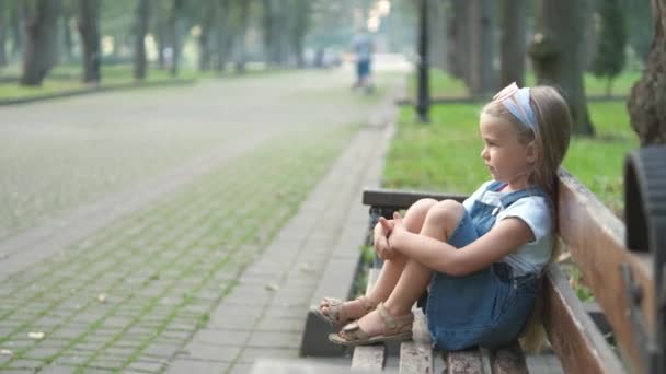 小さな深刻な子供の女の子一人で夏の公園のベンチに座って — ストック動画