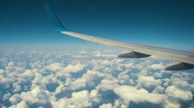 Mavi gökyüzünde beyaz kabarık bulutların üzerinde uçan jet uçağı kanadının görüntüsü. Seyahat ve hava taşımacılığı kavramı