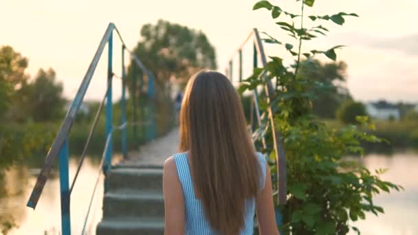 Utsikt bakifrån av ung långhårig kvinna i sommarklänning går uppför trappan utomhus i kvällsparken vid solnedgången — Stockvideo