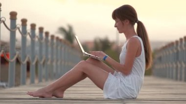 Genç bir kadın sıcak bir yaz akşamında dizüstü bilgisayarında internette geziniyor. Uzak çalışma ve öğrenim kavramı