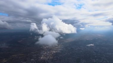 Uzak şehrin yüksek irtifasındaki uçak penceresinden hava manzarası beyaz kabarık kümülüs bulutlarıyla kaplı.