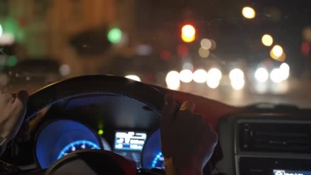 Nahaufnahme des Zeigers des Fahrers mit digitaler Uhr, die die Uhrzeit überprüft und das Lenkrad des fahrenden Autos mit verschwommener Straßenbeleuchtung im Hintergrund in der Nacht hält — Stockvideo
