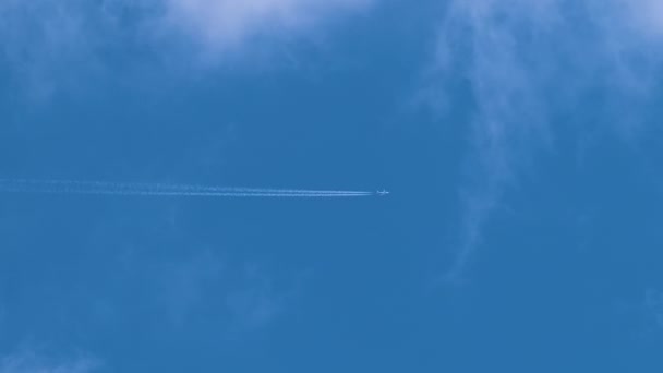 Avião de passageiros distantes voando em alta altitude no céu azul com nuvens brancas deixando vestígios de fumaça de contrail para trás. Conceito de viagem aérea — Vídeo de Stock