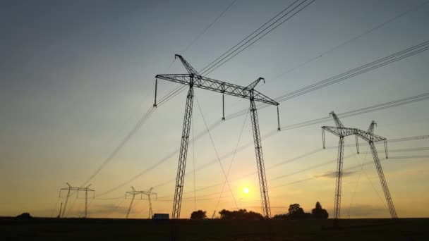 Ciemna sylwetka wież wysokiego napięcia z liniami elektroenergetycznymi o wschodzie słońca — Wideo stockowe