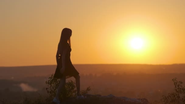 Mörk siluett av en ung kvinna hoppar med upphöjda händer på en sten njuter av solnedgången utsikt utomhus på sommaren — Stockvideo