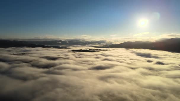 Vista aérea del paisaje por encima de las nubes de niebla de movimiento rápido que cubren las colinas de montaña al atardecer — Vídeo de stock