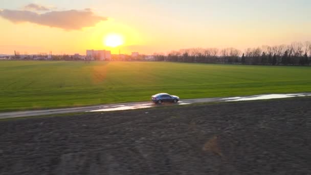 Widok z powietrza na samochód sedana jadący szybko po polnej drodze o zachodzie słońca. Podróżowanie według koncepcji pojazdu — Wideo stockowe