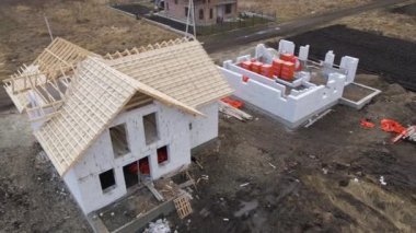 Havalandırılmış hafif beton duvarları ve yapım aşamasındaki ahşap çatı iskeleti olan bitmemiş özel evin havadan görüntüsü.