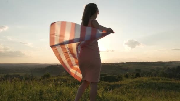 Jovem posando com bandeira nacional dos EUA ao ar livre ao pôr do sol. Menina positiva celebrando o dia da independência dos Estados Unidos — Vídeo de Stock