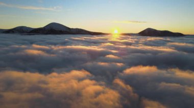 Ufuktaki Karpat dağlarının uzak karanlık zirveleriyle beyaz yoğun sis üzerinde canlı gün doğumunun havadan görüntüsü