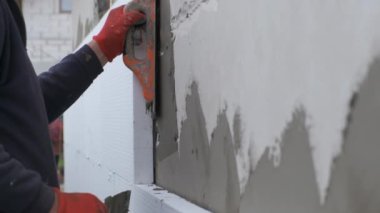 İnşaat işçisi ev duvarını yapışkan çimento yapıştırıcısıyla kaplıyor berore termal koruma için köpük yalıtım çarşafları yerleştiriyor.