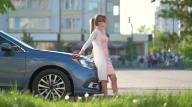 Bir yaz caddesinde arabasının yanında sıcak bir günün tadını çıkaran günlük kıyafetli mutlu bir kadın sürücü. Seyahat ve ulaşım kavramı