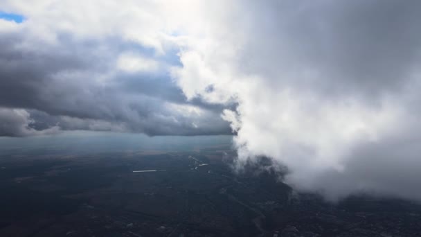 Vista aérea desde la ventana del avión a gran altitud de la ciudad distante cubierta de nubes de cúmulos hinchados que se forman antes de la tormenta — Vídeos de Stock
