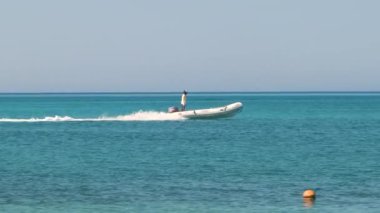 Mavi deniz suyunun dalgalı yüzeyi ve durgun dalgalarda hızlı yüzen beyaz sürat teknesiyle deniz manzarası.