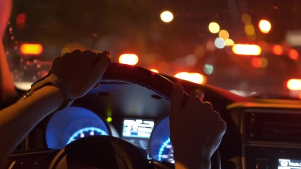 Close up de mãos de motorista segurando volante carro de condução com luzes de rua da cidade borradas no fundo à noite — Vídeo de Stock