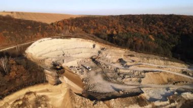 Kazı makineleri ve çöp kamyonlarıyla inşaat endüstrisi için kumtaşı malzemelerinden oluşan açık maden manzarası. Madencilik ve kullanışlı mineral üretiminde ağır ekipman