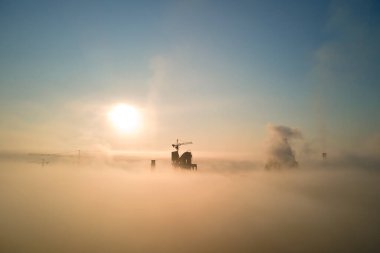 Beton yapılı çimento fabrikasının havadan görünüşü ve sisli bir akşamda endüstriyel üretim alanında kule vinci. Üretim ve küresel sanayi kavramı.