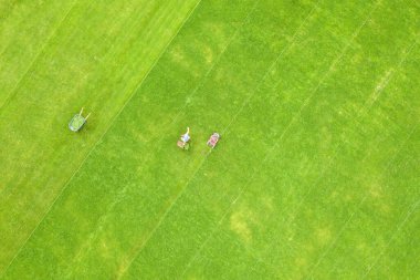 Yazın futbol sahasında çimenleri biçen ve çim biçen küçük işçi figürünün havadan görünüşü..