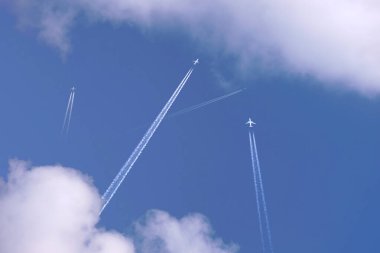 Many distant passenger jet planes flying on high altitude on clear blue sky leaving white smoke trace of contrail behind. Busy air transportation concept. clipart