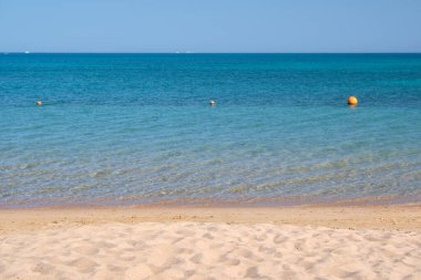 Mavi deniz suyunun yüzeyi ve küçük dalgalı dalgaların sarı kumsala çarptığı deniz burnu. Seyahat ve tatil kavramı.