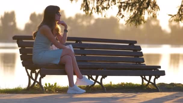 Solitario giovane donna seduta da sola sulla riva del lago panchina godendo calda serata estiva. Benessere e relax nella natura — Video Stock