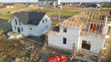 Havalandırılmış hafif beton duvarları ve yapım aşamasındaki ahşap çatı iskeleti olan bitmemiş özel evin havadan görüntüsü.