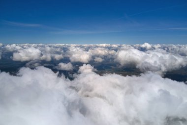 Dünya 'nın yüksek irtifasındaki uçak penceresinden hava manzarası beyaz kabarık kümülüs bulutlarıyla kaplı.