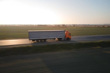 Bulanık hızlı hareket eden yarı kamyonun hava görüntüsü. Kargo karavanıyla birlikte akşamları otobanda mal taşırken görülüyor. Teslimat ulaşım ve lojistik kavramı