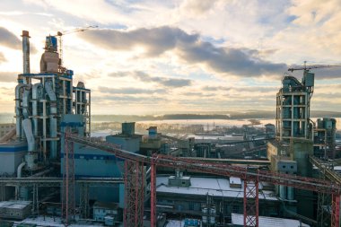 Yüksek fabrika yapısına sahip çimento fabrikasının hava manzarası ve günbatımında endüstriyel üretim alanında kule vinci.