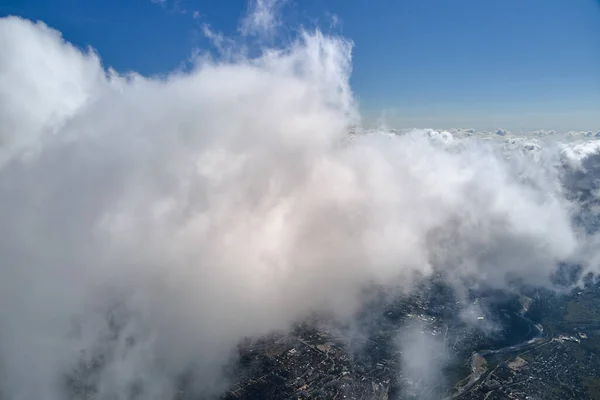 Aerial view from airplane window at high altitude of distant city covered with puffy cumulus clouds forming before rainstorm — Stock Photo, Image