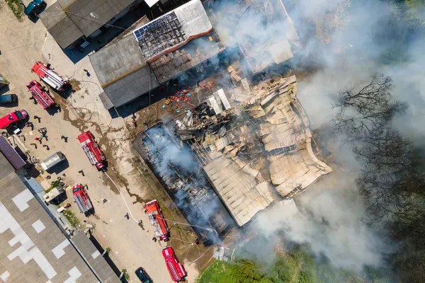 Воздушный обзор пожарных, тушащих разрушенное здание с разрушенной крышей и поднимающимся темным дымом — стоковое фото