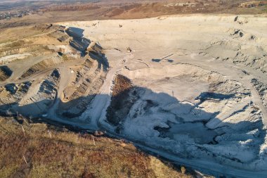 Kazı makineleri ve çöp kamyonlarıyla inşaat endüstrisi için kumtaşı malzemelerinden oluşan açık maden manzarası. Madencilik ve kullanışlı mineral üretiminde ağır ekipman