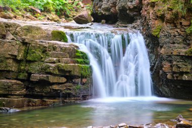 Yazın yağmur ormanlarında kayalık kayalıklardan dökülen beyaz köpüklü suyla dağ nehrindeki muhteşem şelale manzarası.