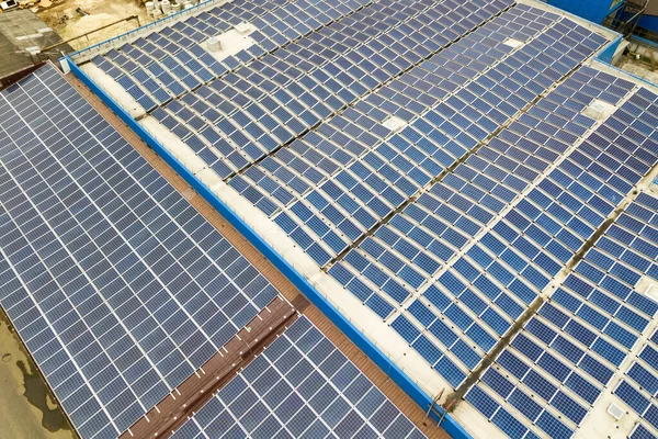 Вид з повітря на сонячну електростанцію з блакитними фотоелектричними панелями, встановленими на промисловий будівельний дах — стокове фото