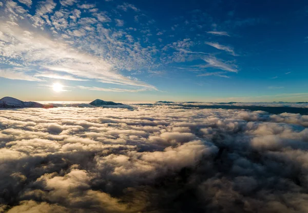 Vzdušný pohled na zářící východ slunce nad bílými hustými mraky se vzdálenými temnými horami na obzoru — Stock fotografie