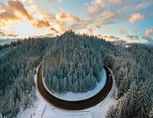 Вид с воздуха на зимний пейзаж с заснеженными горными холмами и извилистой лесной дорогой утром — стоковое фото