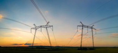 Gün batımında elektrik hatları olan yüksek voltaj kuleleri.