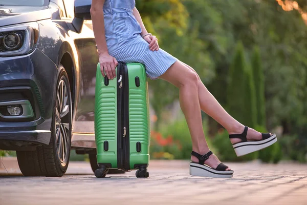 Primer plano de las piernas femeninas jóvenes sentadas en el bolso de la maleta al lado del coche. Concepto de viajes y vacaciones — Foto de Stock