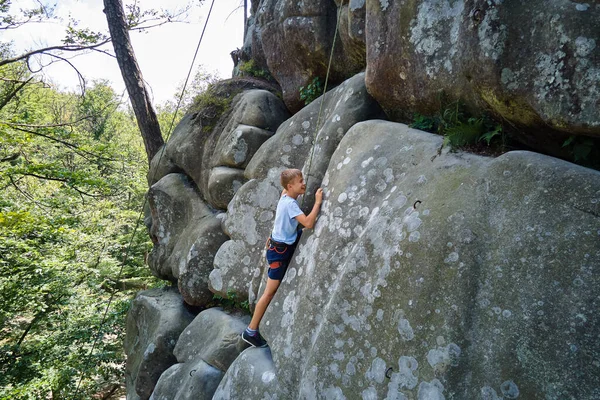 Déterminé garçon grimpeur escalade mur escarpé de montagne rocheuse. Enfant surmonter la route difficile. S'engager dans des sports extrêmes et le concept de passe-temps d'escalade — Photo