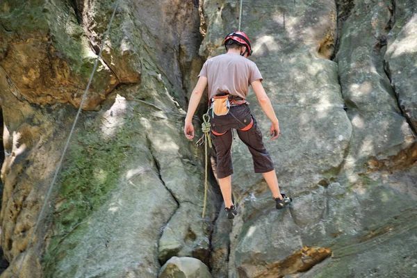 Odhodlaný horolezec šplhá po příkré stěně skalnaté hory. Sportovec překonává obtížnou cestu. Zapojení do extrémních sportů a horolezectví hobby koncept — Stock fotografie