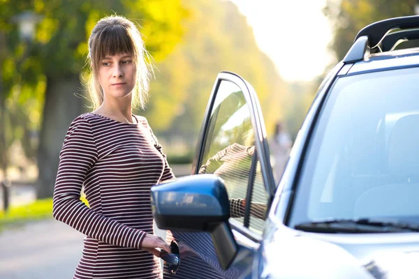 Счастливая молодая женщина-водитель наслаждается теплым летним днем, стоя рядом со своей машиной на городской улице. Концепция путешествий и отдыха — стоковое фото